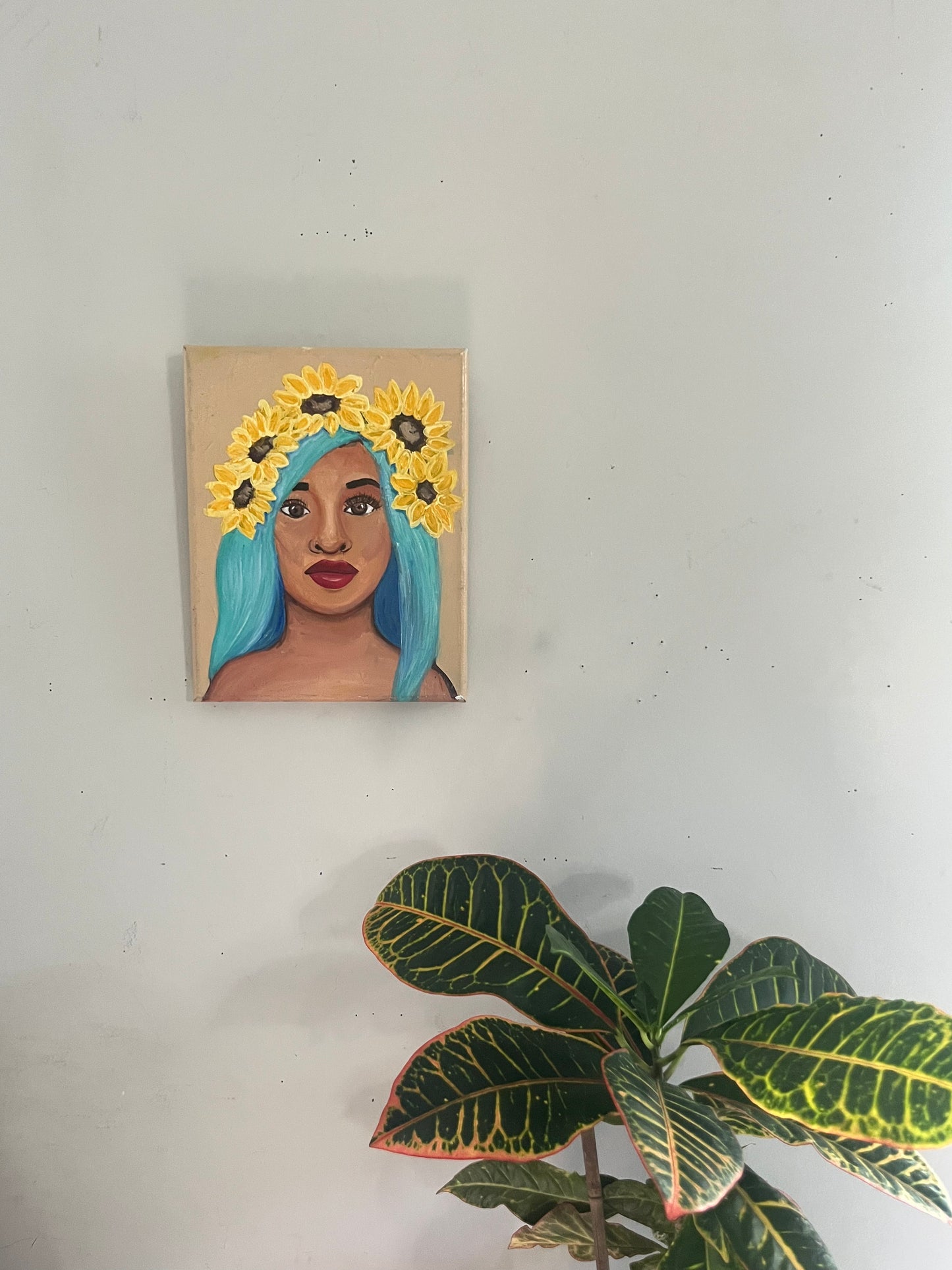 Canvas painting of a Black woman with flowers in their hair on a white wall.