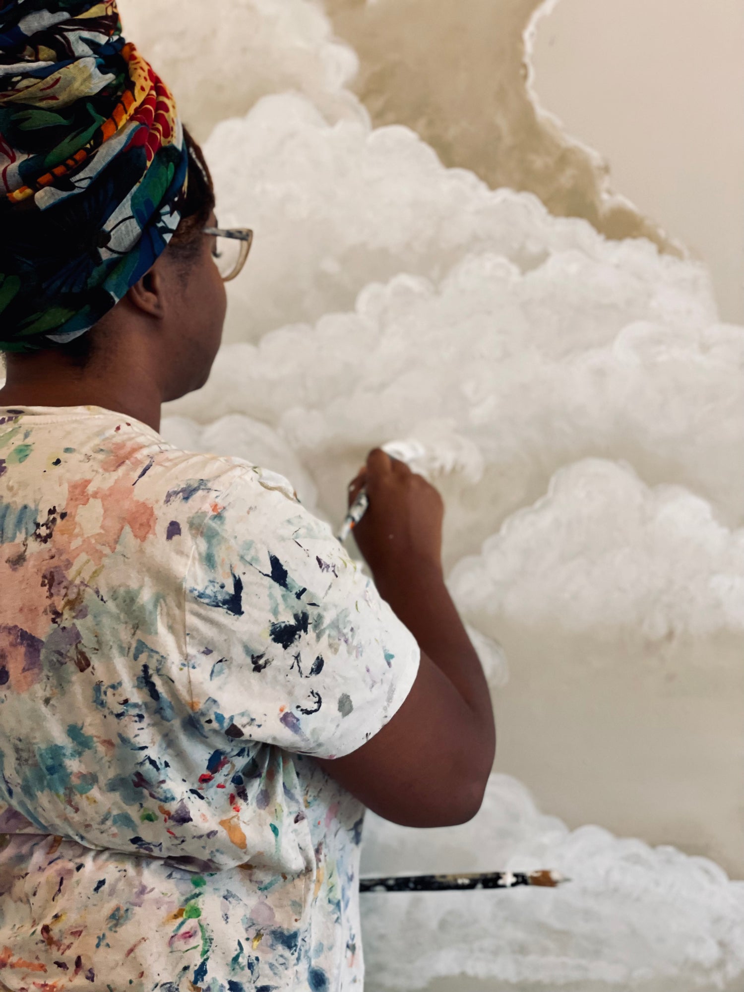 Black woman artists, Bri simpson, is  painting a cloud mural on a wall.